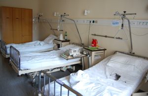 3 leere Krankenhausbetten mit weißen Laken - im Hintergrund dre hellbraune Schränke